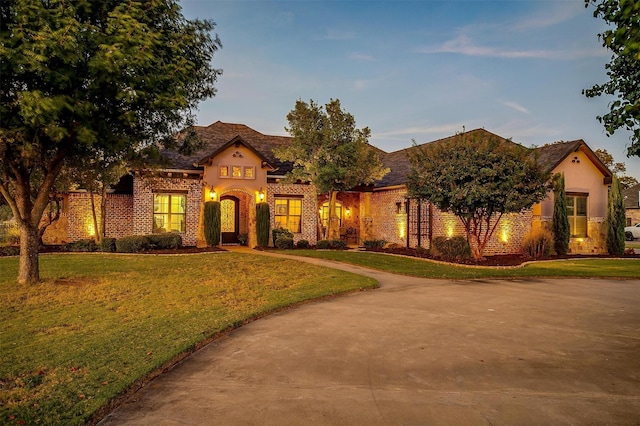 mediterranean / spanish-style house with a yard, brick siding, concrete driveway, and stucco siding