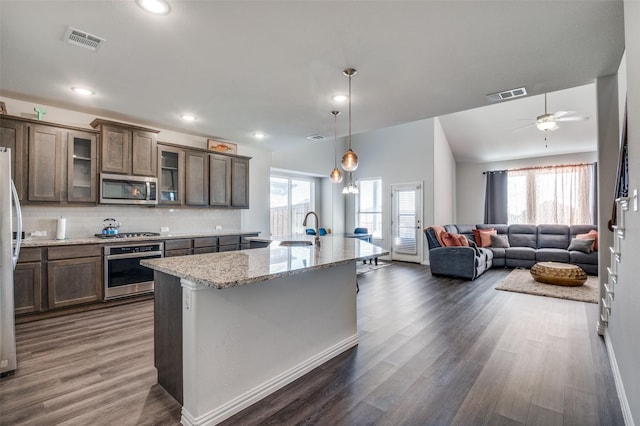 kitchen with sink, light stone counters, an island with sink, pendant lighting, and stainless steel appliances