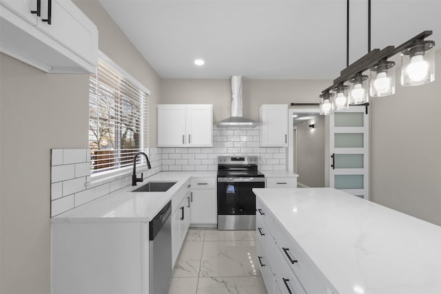 kitchen featuring wall chimney exhaust hood, sink, white cabinetry, decorative light fixtures, and appliances with stainless steel finishes