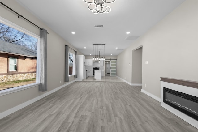 unfurnished living room featuring an inviting chandelier, light hardwood / wood-style flooring, and a barn door