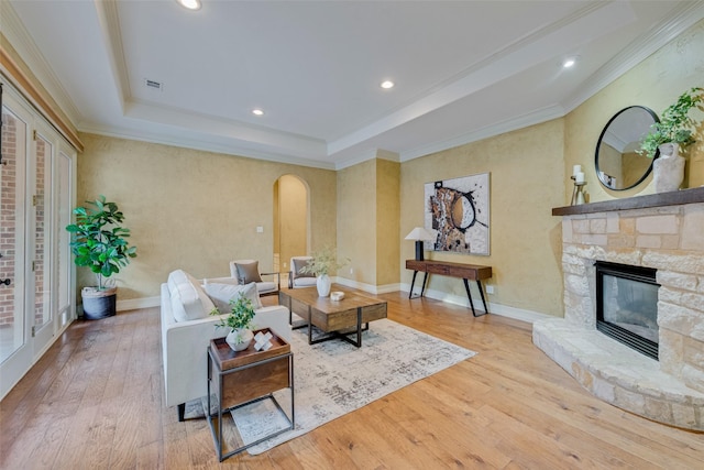 living room featuring crown molding, a fireplace, light hardwood / wood-style floors, and a tray ceiling