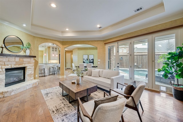 living room with a fireplace, a raised ceiling, and light wood-type flooring