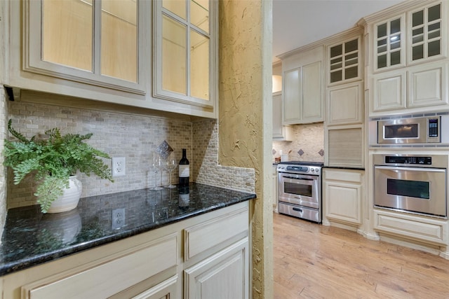 kitchen with stainless steel appliances, decorative backsplash, dark stone counters, and light hardwood / wood-style flooring