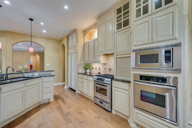 kitchen with sink, appliances with stainless steel finishes, hanging light fixtures, cream cabinetry, and light wood-type flooring