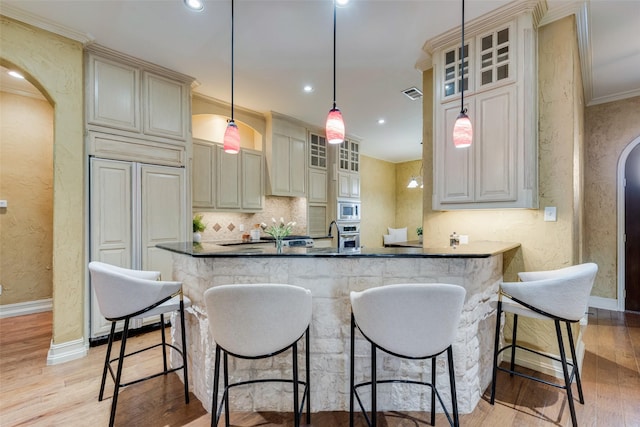 kitchen featuring pendant lighting, stainless steel appliances, tasteful backsplash, cream cabinetry, and light wood-type flooring