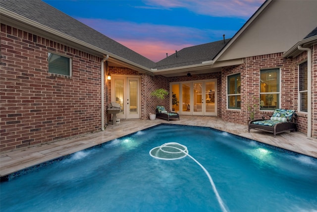 pool at dusk with french doors, pool water feature, a grill, and a patio