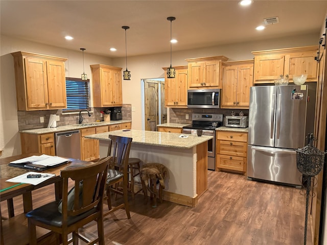 kitchen with pendant lighting, dark wood-type flooring, appliances with stainless steel finishes, light stone counters, and a kitchen island