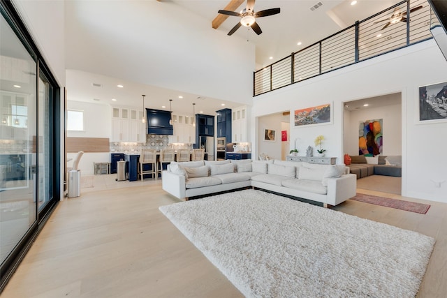 living area with visible vents, ceiling fan, light wood-style flooring, and a towering ceiling
