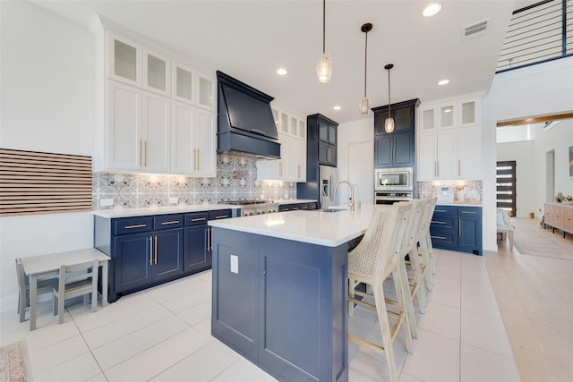 kitchen featuring appliances with stainless steel finishes, light tile patterned floors, premium range hood, and blue cabinets
