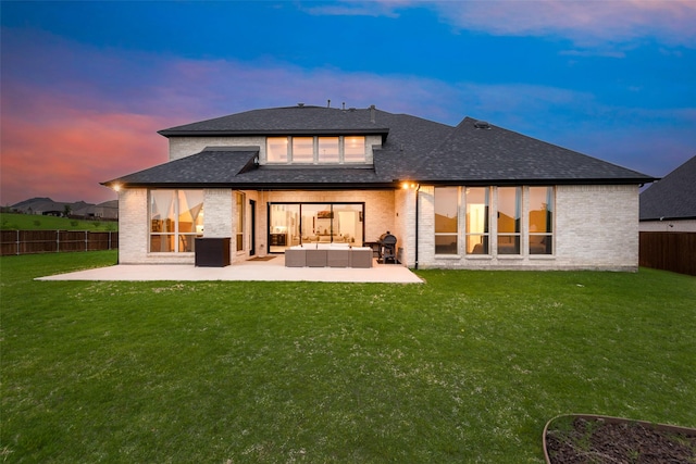 back of property at dusk with an outdoor living space, a lawn, a patio area, brick siding, and fence