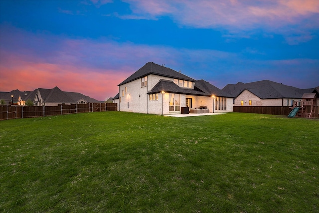back of house at dusk featuring a lawn, a patio, a fenced backyard, and a playground