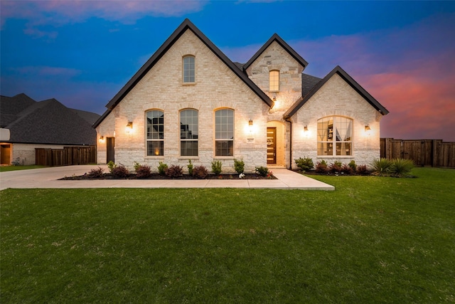 french country style house featuring brick siding, fence, a front yard, and concrete driveway