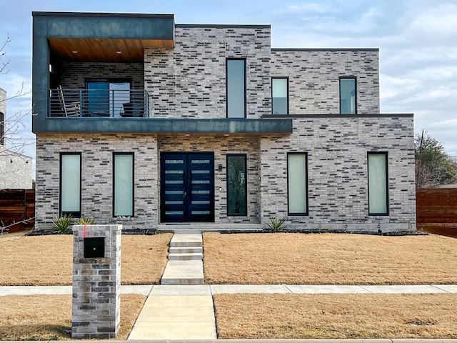 contemporary home featuring brick siding, fence, and a balcony