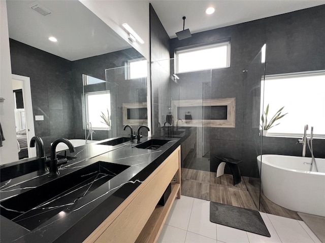 bathroom featuring double vanity, a walk in shower, a soaking tub, and a sink