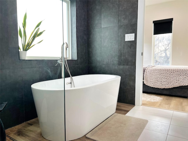 bathroom featuring a freestanding tub, tile walls, ensuite bathroom, and tile patterned floors