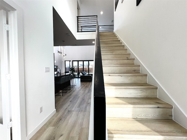 staircase with wood finished floors, recessed lighting, baseboards, and a high ceiling