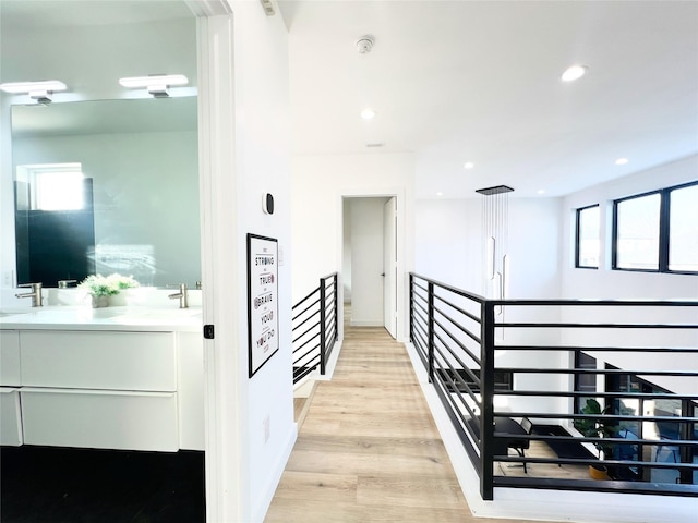 corridor with recessed lighting, a sink, light wood-style flooring, and an upstairs landing