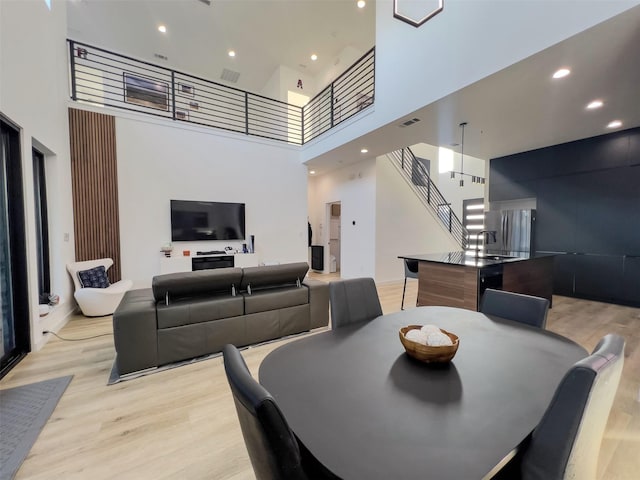 dining room with visible vents, stairs, light wood finished floors, a high ceiling, and recessed lighting