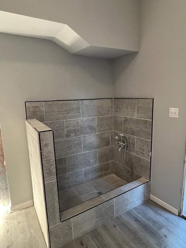 bathroom featuring baseboards, wood finished floors, and a tile shower