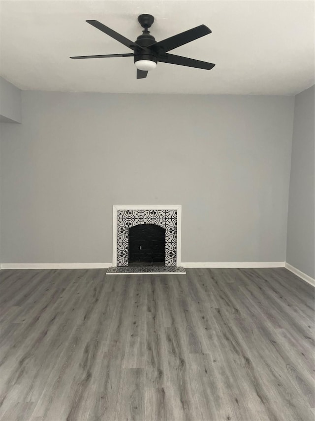 unfurnished living room with a tile fireplace, baseboards, ceiling fan, and wood finished floors