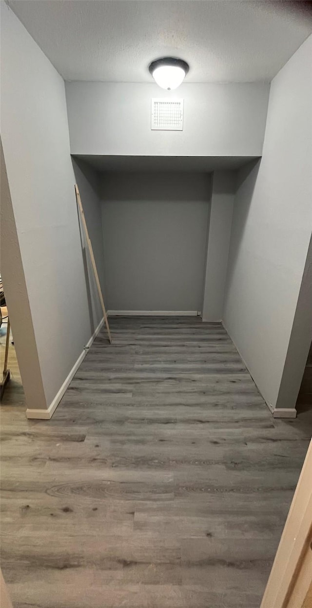 finished basement featuring visible vents, a textured ceiling, baseboards, and wood finished floors