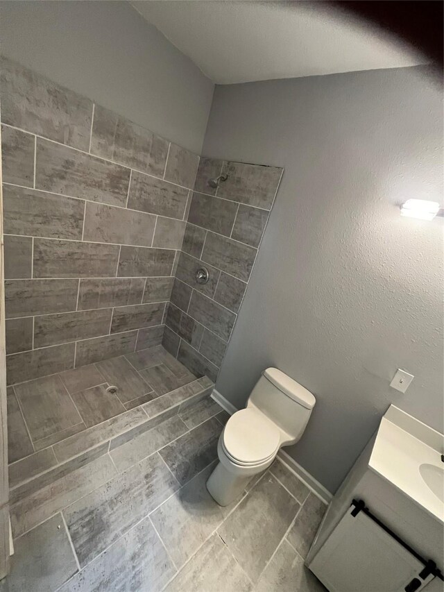 bathroom featuring toilet, vanity, and a tile shower