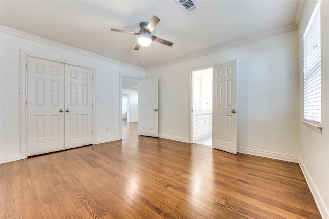 unfurnished bedroom with ensuite bathroom, crown molding, wood-type flooring, a closet, and ceiling fan