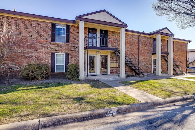 view of front of property featuring stairs, brick siding, and a front lawn