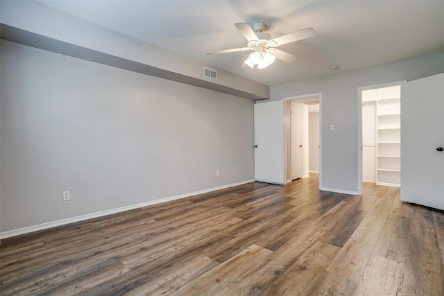 unfurnished bedroom featuring wood finished floors, visible vents, baseboards, a spacious closet, and a closet