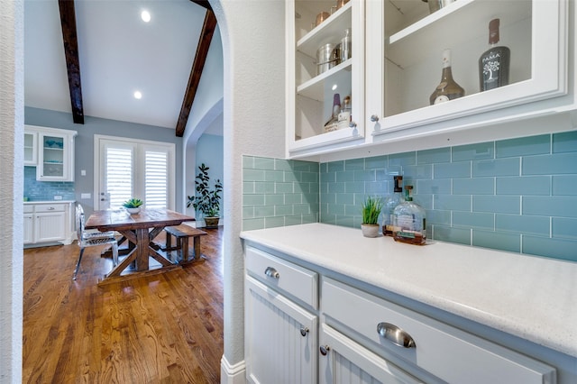 kitchen featuring backsplash, hardwood / wood-style floors, lofted ceiling with beams, and white cabinets