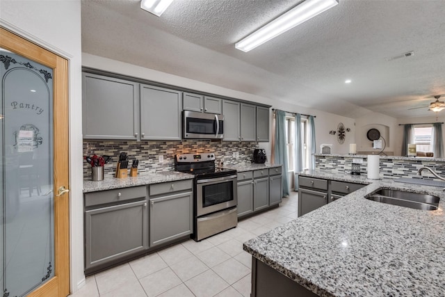 kitchen with sink, gray cabinetry, stainless steel appliances, light stone countertops, and backsplash