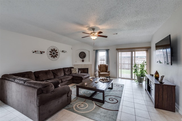 tiled living room with ceiling fan, vaulted ceiling, a textured ceiling, and a fireplace