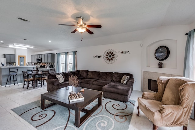 tiled living room featuring ceiling fan, a textured ceiling, and a fireplace