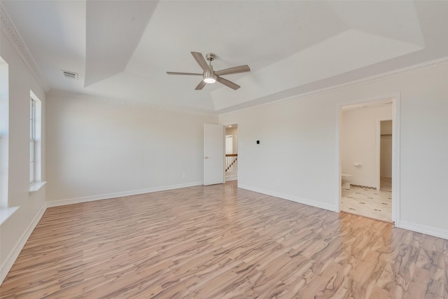 empty room with ceiling fan, ornamental molding, a tray ceiling, and light wood-type flooring