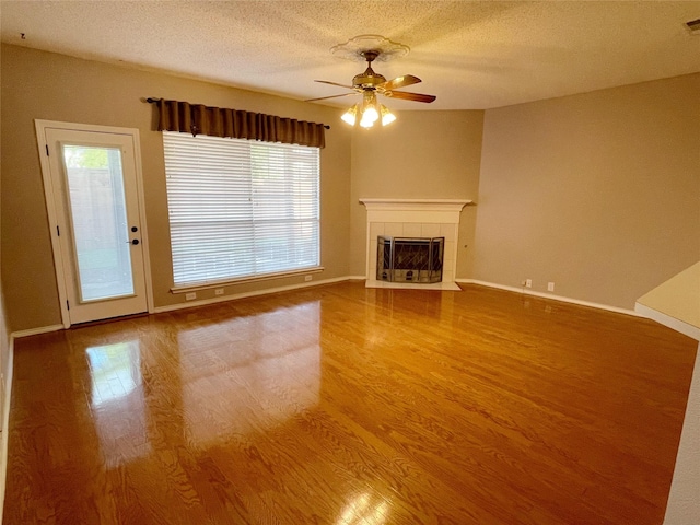 unfurnished living room featuring a tiled fireplace, ceiling fan, wood-type flooring, and a textured ceiling