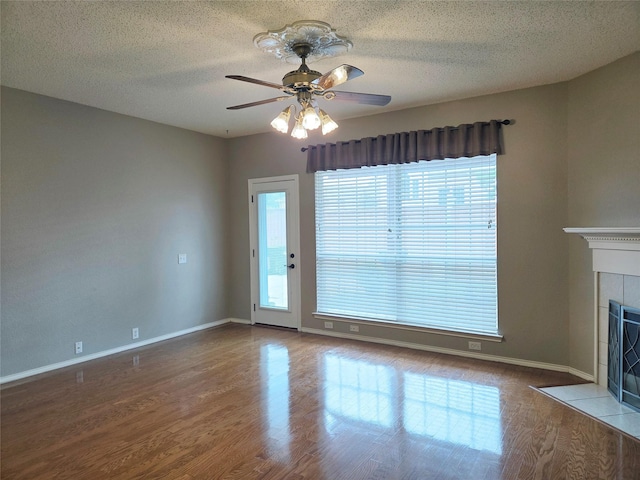 6464 Richmond Dr, Frisco, TX 75035 - unfurnished living room with ceiling fan, wood finished floors, a tiled fireplace, a textured ceiling, and baseboards