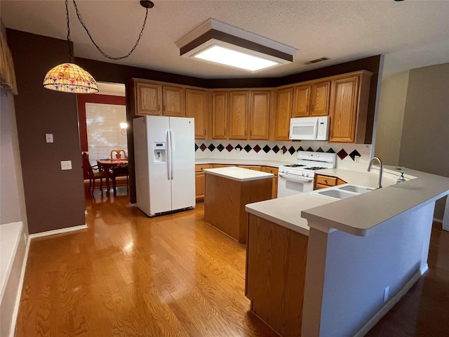 kitchen with sink, kitchen peninsula, pendant lighting, white appliances, and light hardwood / wood-style floors