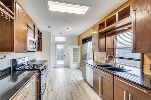 kitchen with appliances with stainless steel finishes, sink, decorative backsplash, dark stone counters, and light hardwood / wood-style flooring