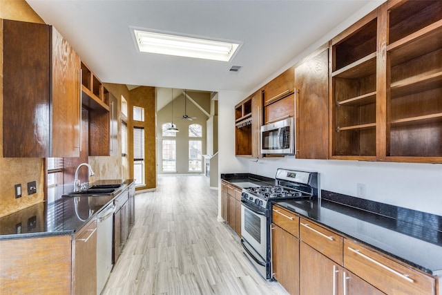 kitchen featuring appliances with stainless steel finishes, sink, dark stone counters, ceiling fan, and light hardwood / wood-style flooring