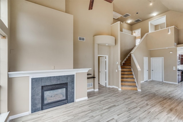 unfurnished living room featuring a tiled fireplace, a towering ceiling, and light hardwood / wood-style floors