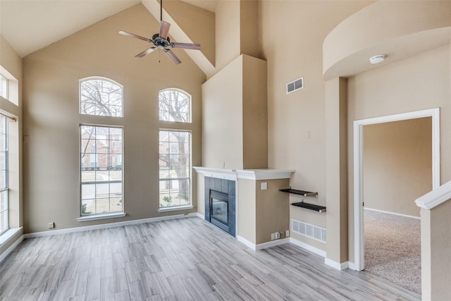 unfurnished living room featuring high vaulted ceiling, a wealth of natural light, a fireplace, and light hardwood / wood-style floors