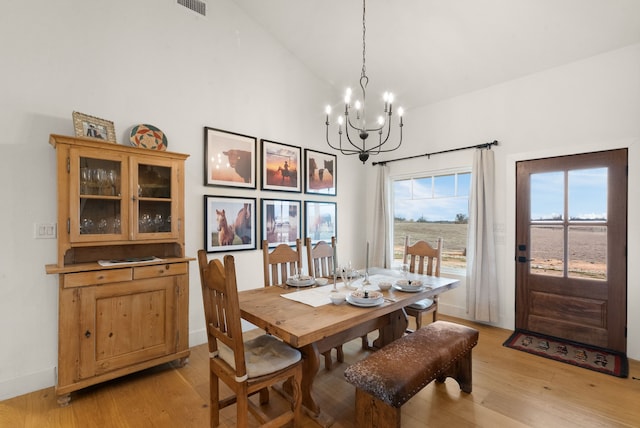 dining area with an inviting chandelier, high vaulted ceiling, and light hardwood / wood-style floors