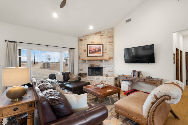 living room featuring ceiling fan, wood-type flooring, a stone fireplace, and high vaulted ceiling