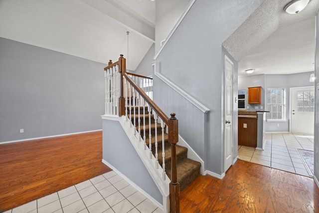 stairs featuring tile patterned flooring, lofted ceiling, and a textured ceiling