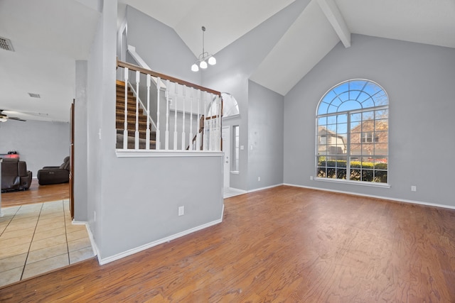 unfurnished living room with beamed ceiling, high vaulted ceiling, ceiling fan with notable chandelier, and hardwood / wood-style floors