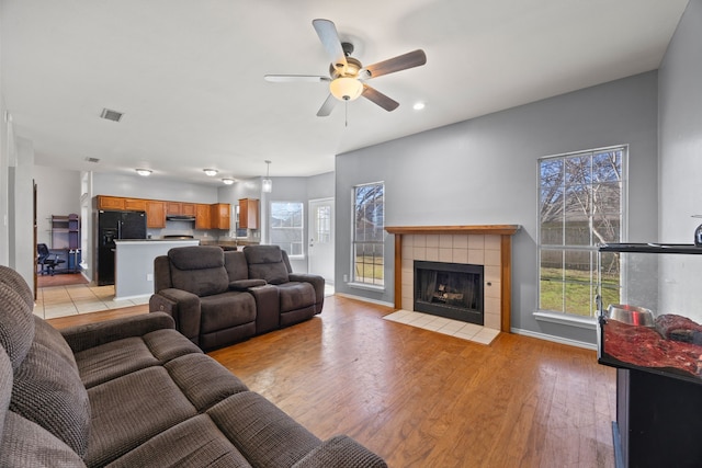 living room featuring a tiled fireplace, light hardwood / wood-style floors, and ceiling fan