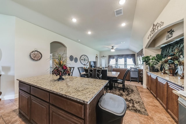 kitchen featuring light stone countertops, a kitchen island, dark brown cabinets, and lofted ceiling