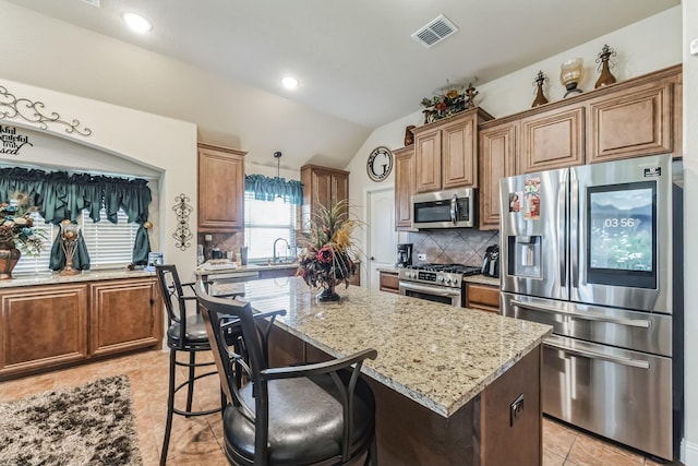 kitchen with light stone counters, appliances with stainless steel finishes, a kitchen island, pendant lighting, and backsplash