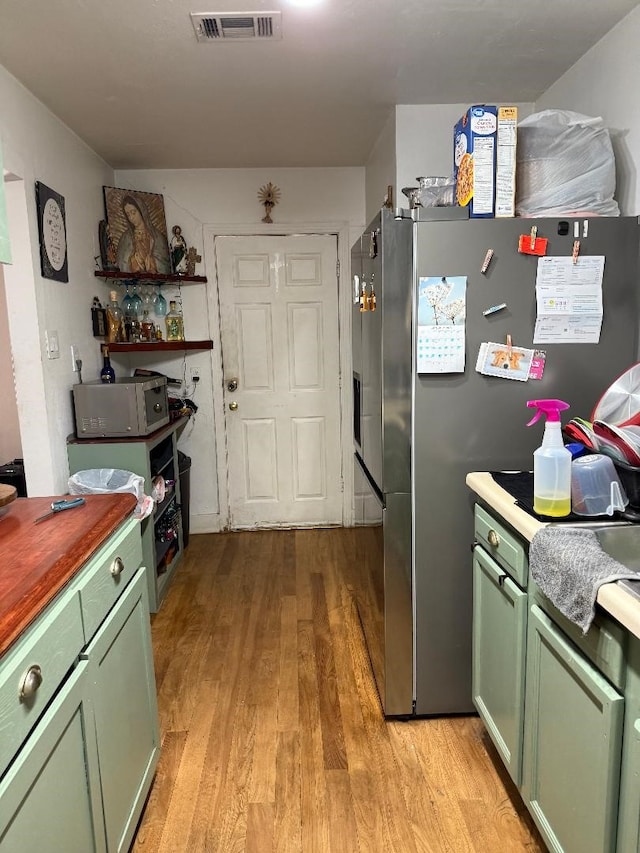 kitchen with stainless steel refrigerator, green cabinets, and light hardwood / wood-style flooring