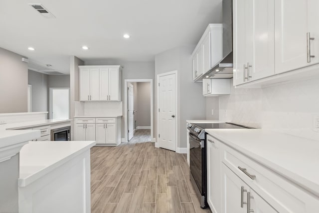 kitchen with electric stove, wall chimney range hood, tasteful backsplash, and white cabinets